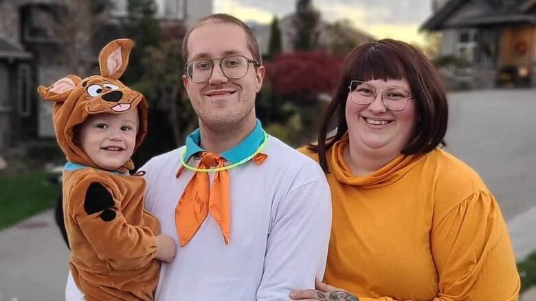 A baby, father and mother are pictured dressed up as Scooby Doo, Fred and Velma from the Scooby Doo franchise.