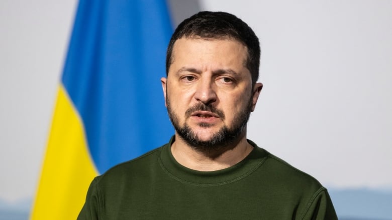 Ukrainian President Volodymyr Zelenskyy stands in front of a Ukrainian flag