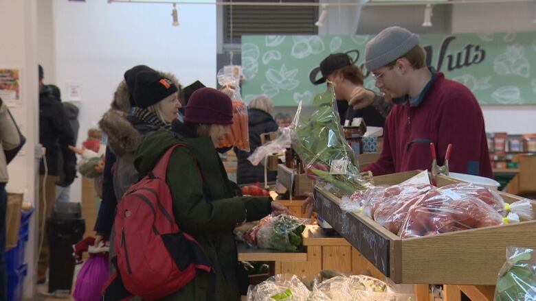 Several people in winter coats and hats shopping for vegetables in a old building 