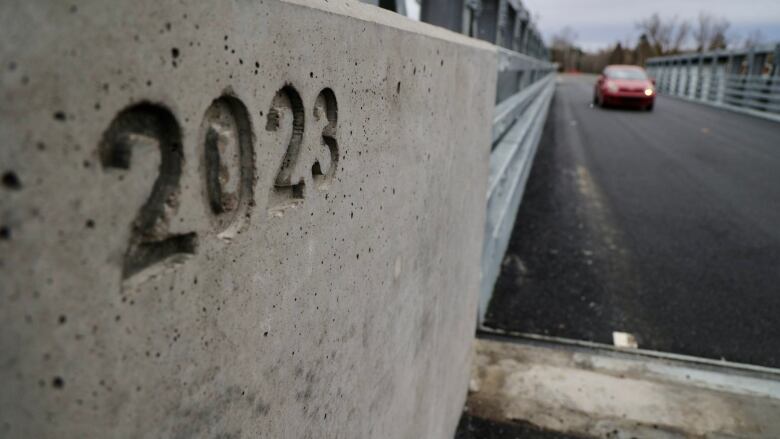 A red car drives across a new two-lane bridge.