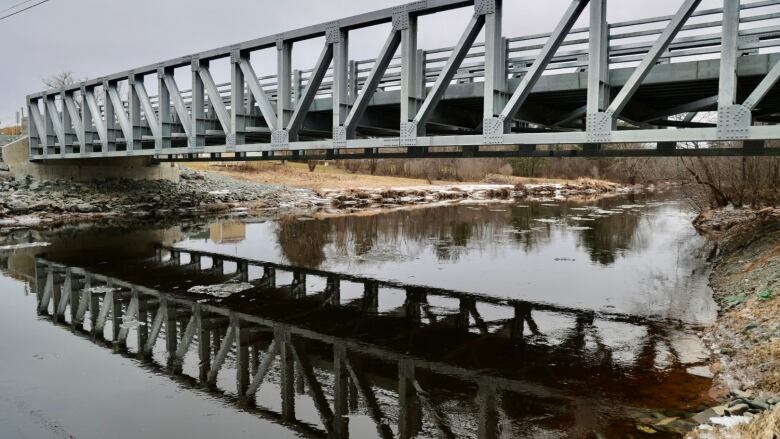 A side view of a metal bridge spanning a river/