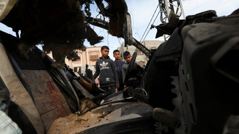 Children inspect the remains of a destroyed car.