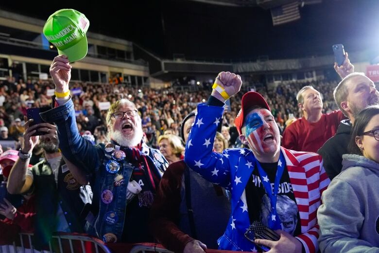 People cheering, one wearing a suit resembling US flag with his face painted in flag colours