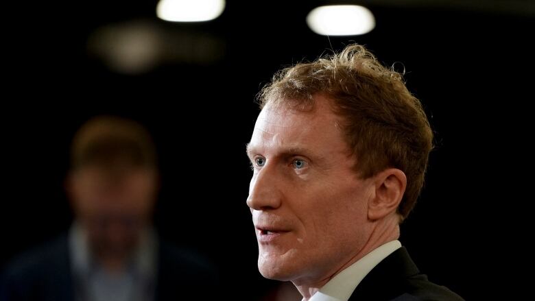 Profile headshot of Immigration Minister Marc Miller, with person standing in the background who is blurred by a shallow depth of field.