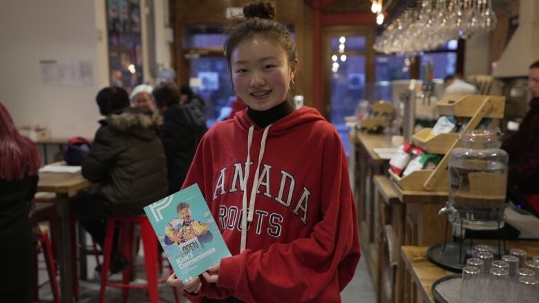 A young woman with dark hair, wearing a red hooded sweatshirt that says 