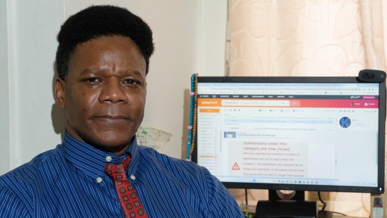 A man poses for a photo beside a computer screen that has an error message on it.