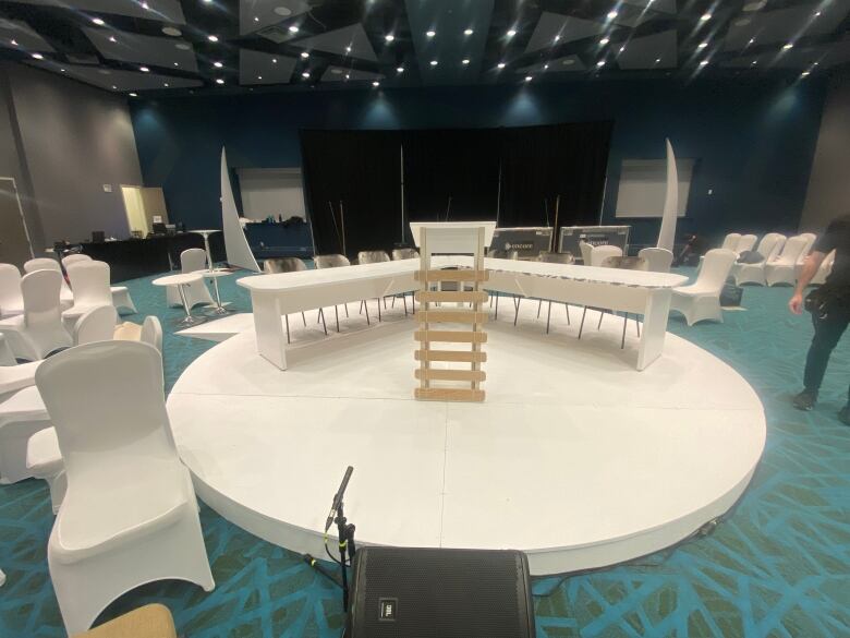 A V-shaped table and sealskin chair sit on a white, flat stage with a podium shaped like a traditional sled. Everything is white. 