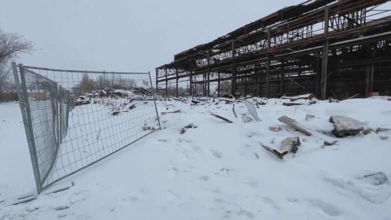 A burnt-out warehouse building can be seen in this photo, with a metal fence around it. Part of the fence has been pulled open.