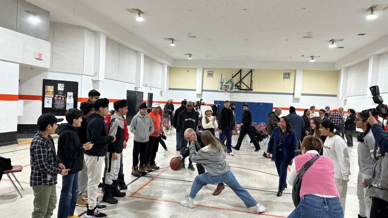 A crowd watches as an older man wearing a suit plays basketball with a younger girl. 