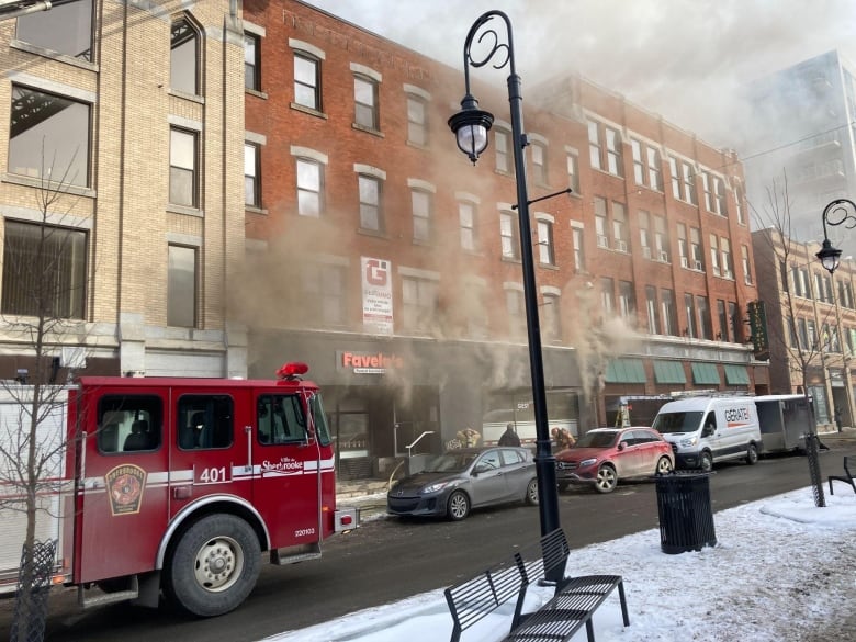 Smoke emerges from a building. A firetruck is parked nearby.