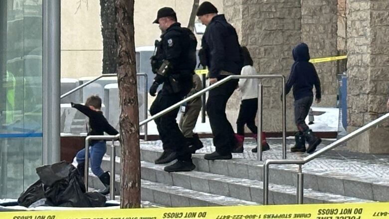 Officers and children walk down the steps of a large building. 