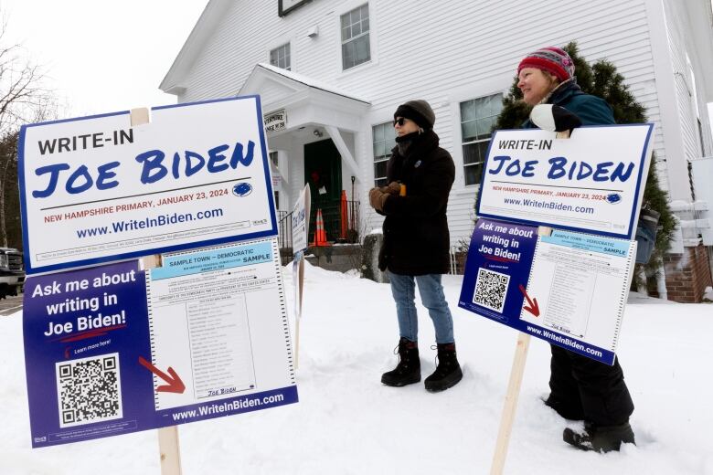 Two people stand in snow in front of a church with signs reading 