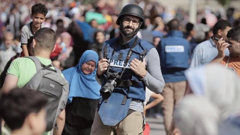 A bearded man with glasses, wearing a black helmet and a blue vest with the word 