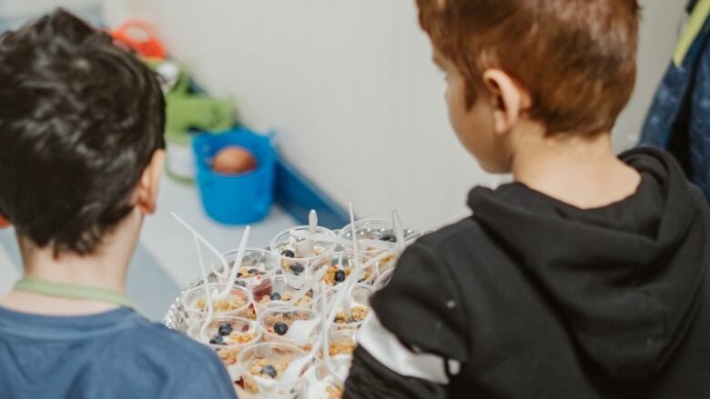 Two students walk with a tray of yogurt cups. 