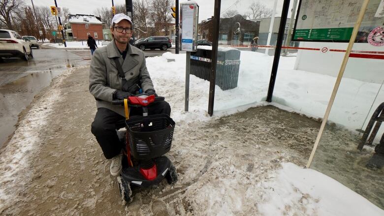 A man wearing a baseball cap sits in a mobility scooter at a bus stop.