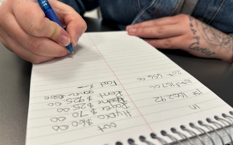 A notebook on a table and someone holding a pen. 