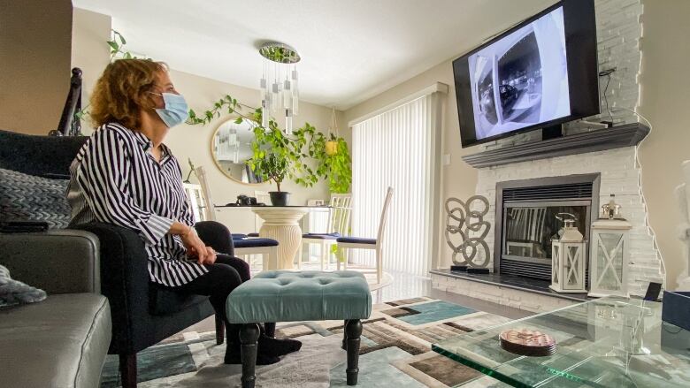 A woman watches doorbell camera footage on a TV in her home.