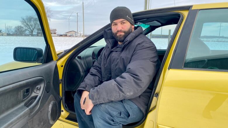 Man sitting in the front seat of a car with the door open.