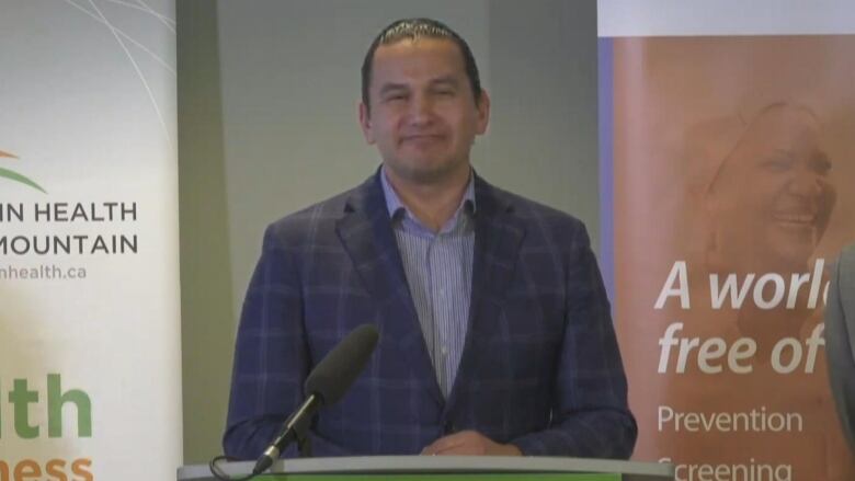 A man is shown standing at a podium.