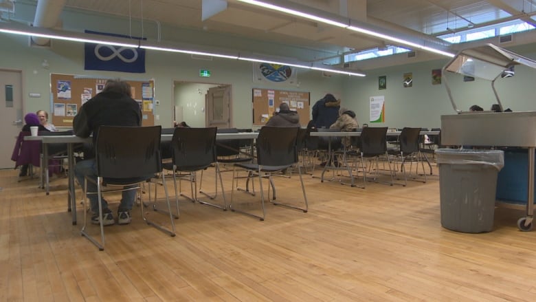 A big room with green walls that has tables and chairs, where people are sitting.