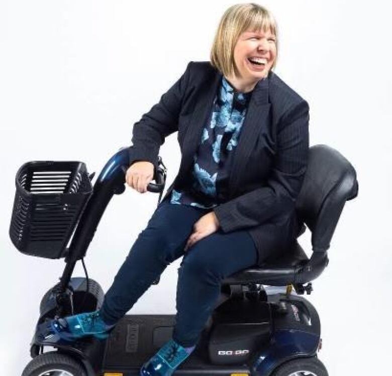 a blonde woman with blue shoes sits in a motorized wheelchair and smiles