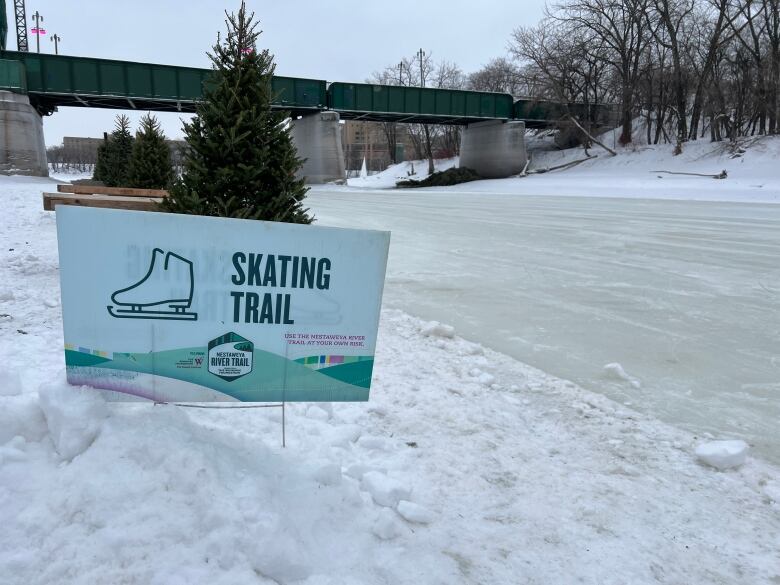 A sign that says 'skating trail' besides a frozen river.