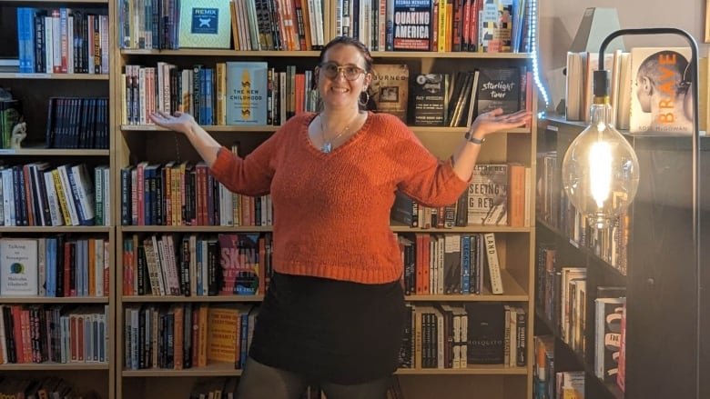 A woman in a red sweater is flanked by shelves of books.