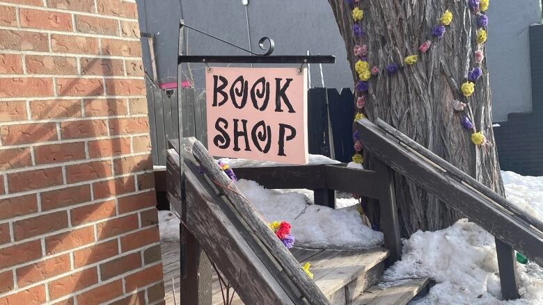 A sign saying Book Shop hangs outside a business stoop, with snow in the background.