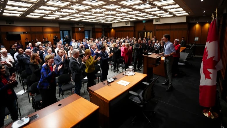 A room full of MPs applaud Prime Minister Justin Trudeau as he stands at a podium to deliver a speech.