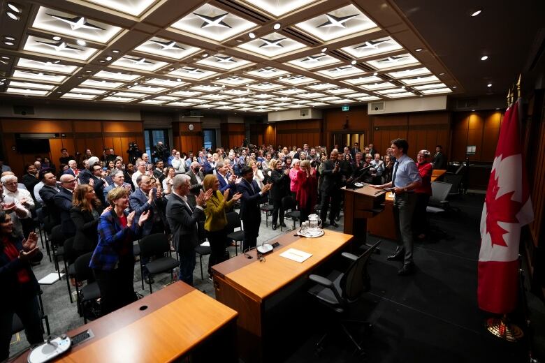 A room full of MPs applaud Prime Minister Justin Trudeau as he stands at a podium to deliver a speech.