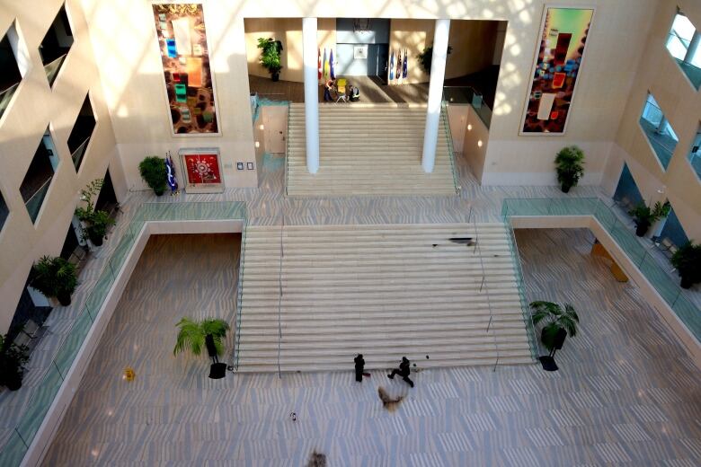 An aerial view of the inside of a large hall with a marble floor where workers are bent over scorch marks.