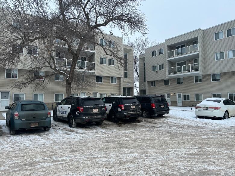 A snowy parking lot with four vehicles parked in it. Two are Edmonton police vehicles. 