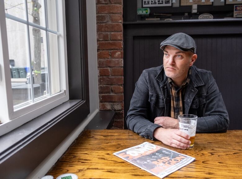 A bearded man sits at a  table in a pub.