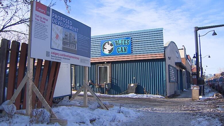 A proposed development sign sits outside of a blue building. 