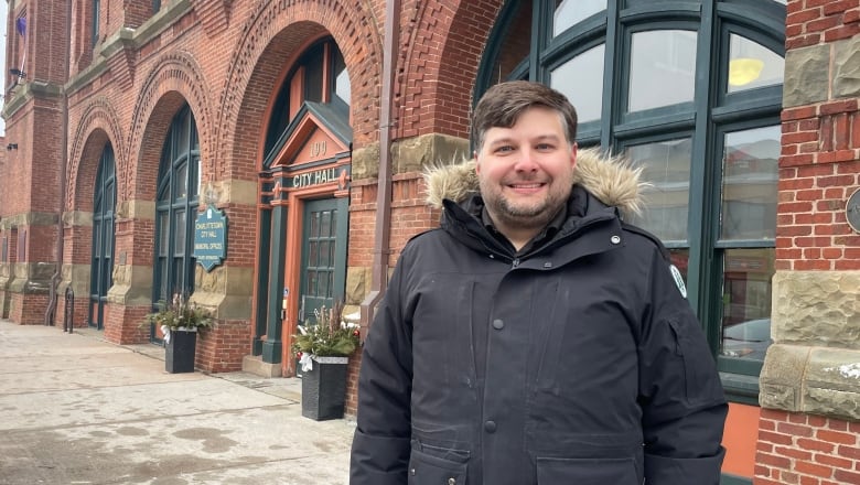 A man in a winter coat stands in front of a sandstone building. 