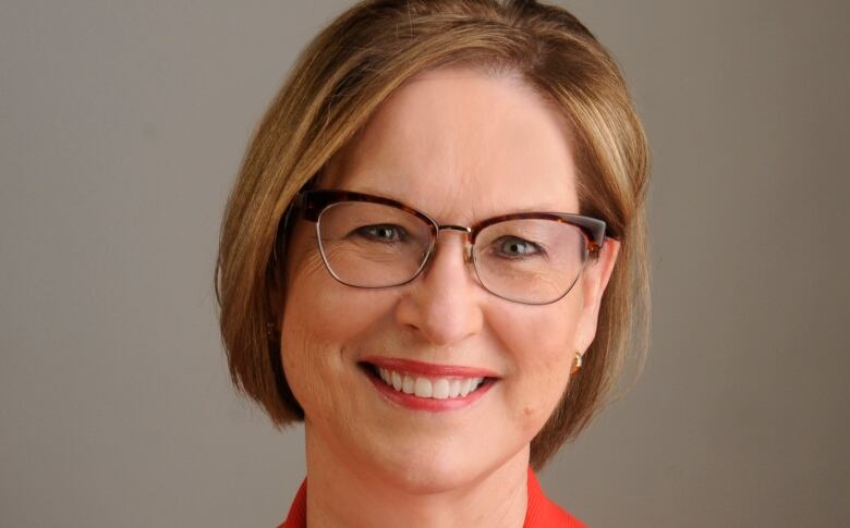 A woman with short hair wearing glasses and a red blazer smiles for a portrait.