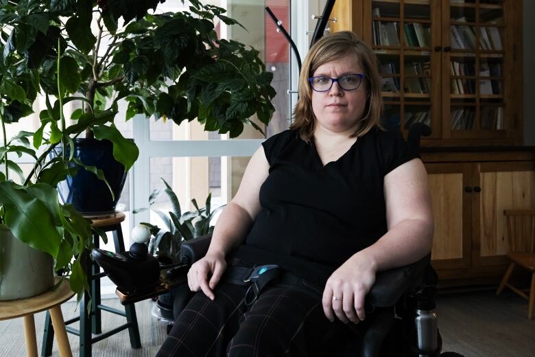 A portrait of a woman wearing glasses and a black shirt sitting in a wheelchair.