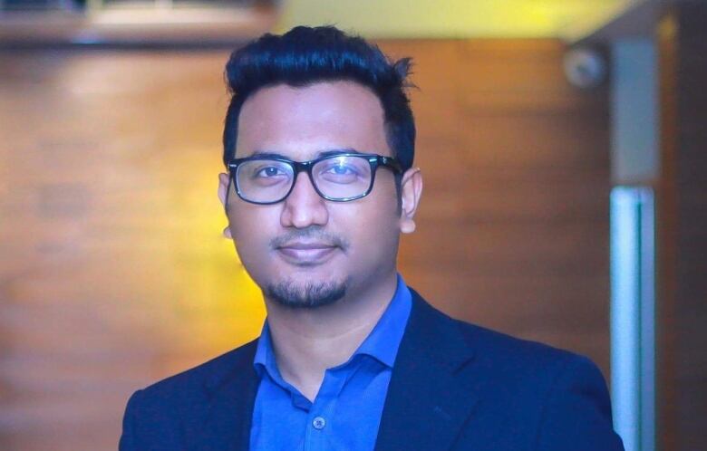  A Bangladeshi man in a blue jacket and shirt smiles at the camera.