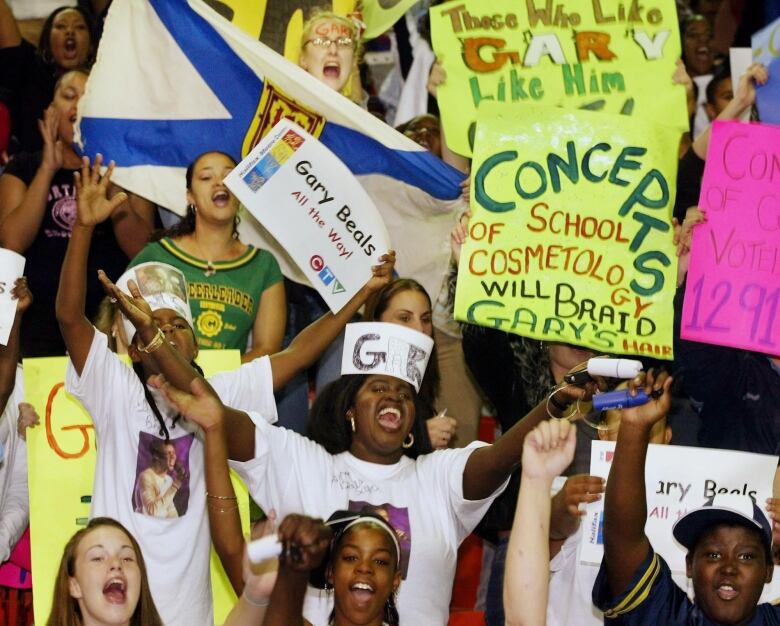 A group of people are shown at a rink cheering on a finalist in a singing competition.