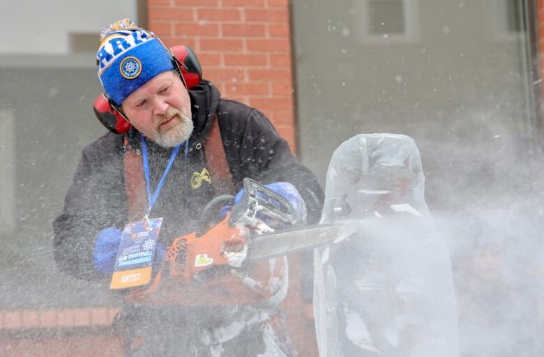 A spray of ice chips is seen as a man carves a block of ice with a chainsaw