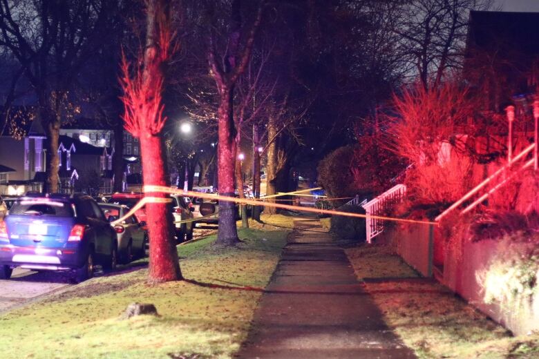 Crime tape blocks off a suburban street, with cars lined up on one side.