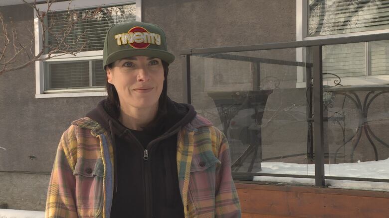 A woman is seen smiling in this close-up picture. She's wearing a dark sweatshirt, a striped jacket, and a cap.