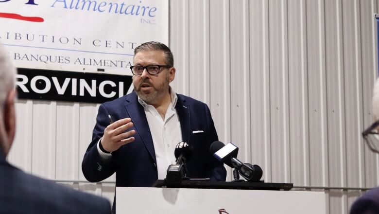 A man in a blue suit wearing glasses with one arm raised speaking at a podium.