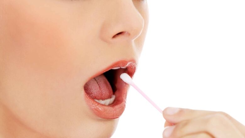 A young woman opens her mouth to take a swab inside.