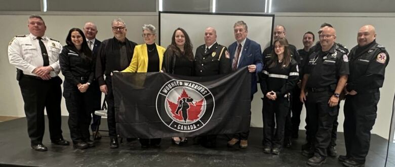 A group of first responders and representatives of Wounded Warriors Canada stands behind a flag.