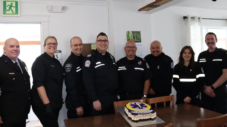 A group of paramedics standing behind a table with a cake.