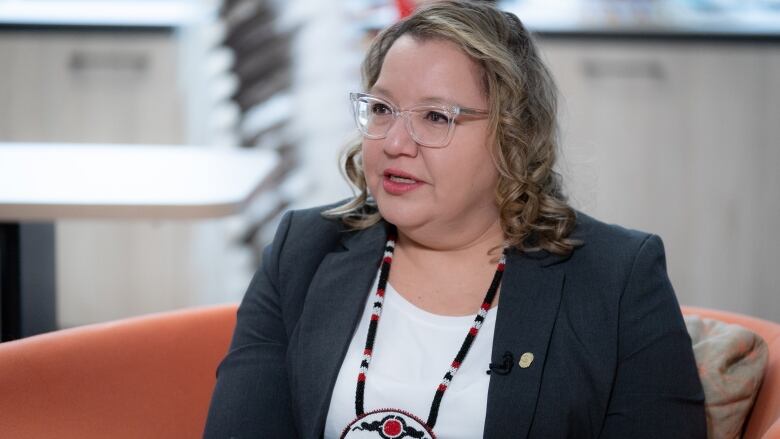 A politician in a suit speaks to a reporter with a beaded medallion with the AFN insignia around her neck.