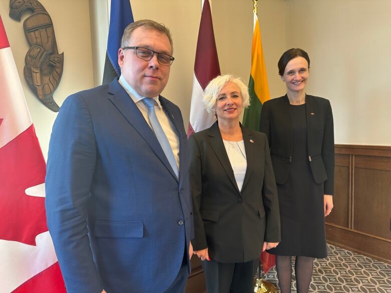 Two women and a man stand in front of flags.