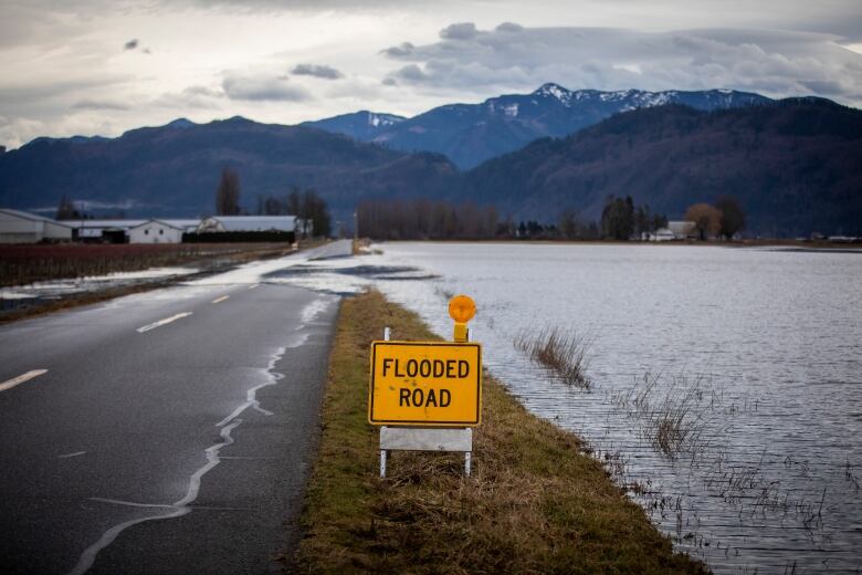 Floodwater covers a farm field and part of a country road. A yellow sign that says 