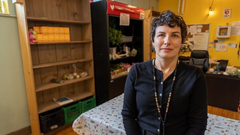 A woman stands in front of a fridge filled with leafy greens and a pantry more sparsely stocked. 